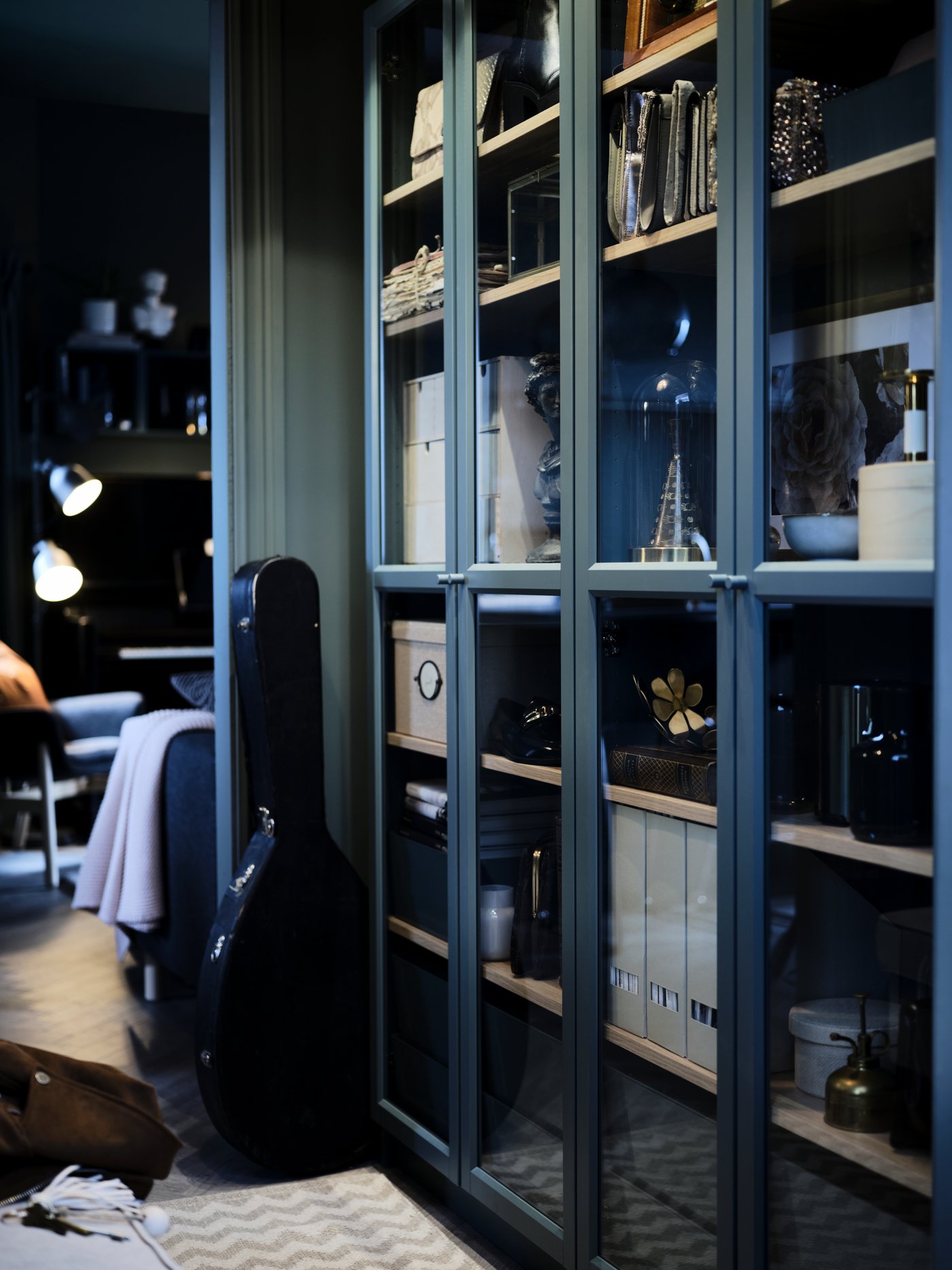 Storage in a row of BILLY glass-door bookcases. Two lamps are lighting up the room in the background.
