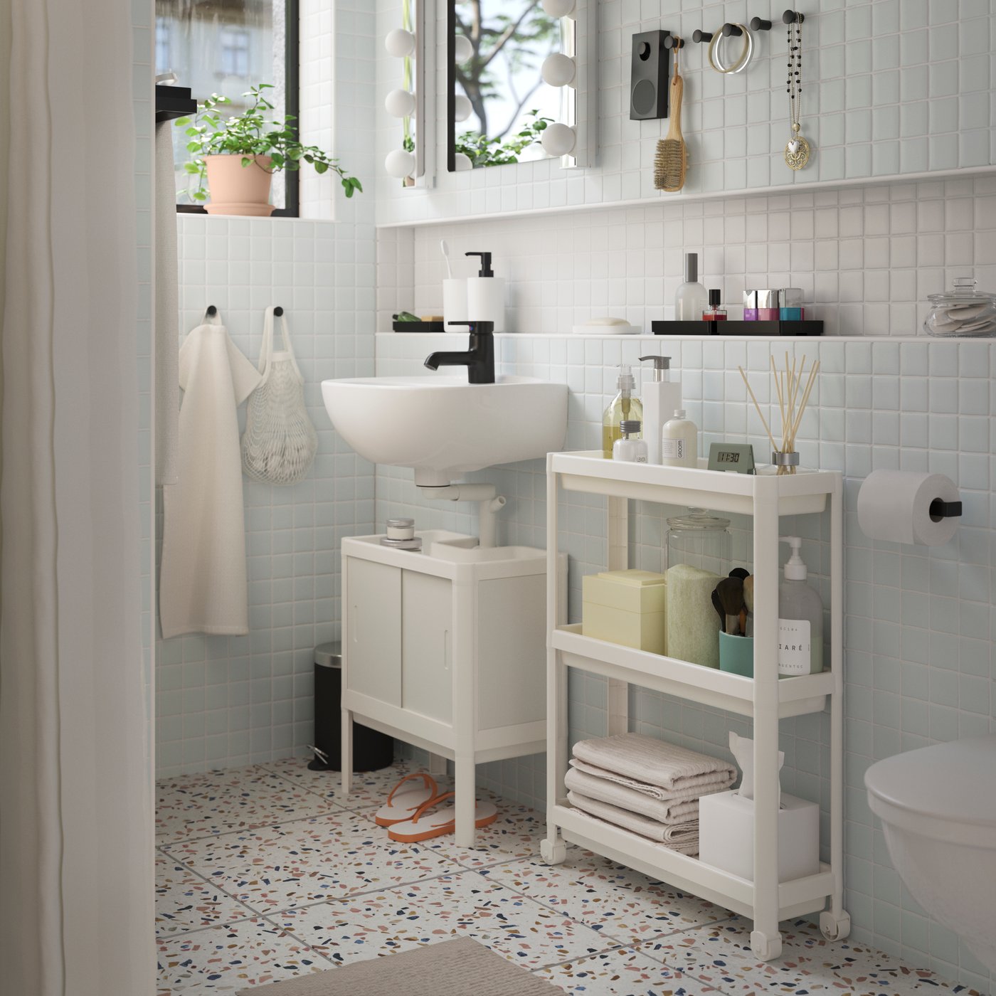 A white LILLTJÄRN/SKATSJÖN bathroom furniture set with a SALJEN tap beside a white VESKEN trolley holding toiletries.
