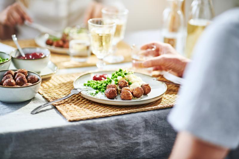 En person sträcker ut en hand med en tallrik köttbullar
