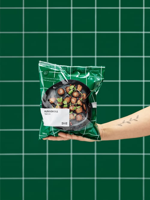 Modern kitchen focus of a person holding a green bag of plant balls in front of a checkered green background. 