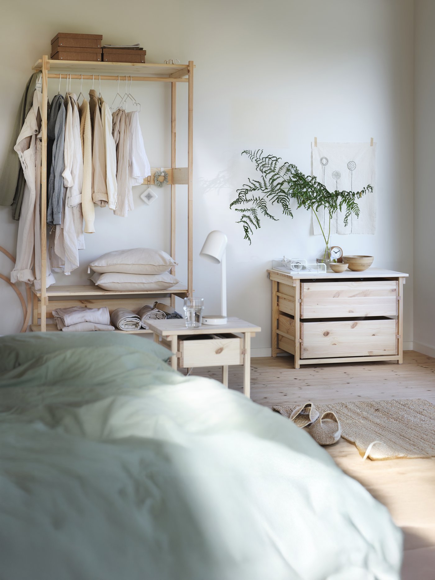 Armadio a vista KRONÖREN in pino con binario e ripiani, collocato in una camera da letto luminosa con pavimenti in legno e tessuti morbidi.