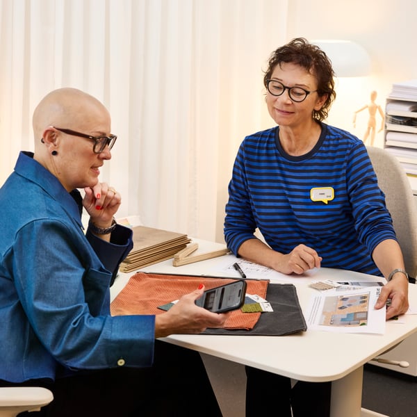 Projektantka wnętrz IKEA siedząca przy biurku z klientką i omawiająca projekt wnętrz.