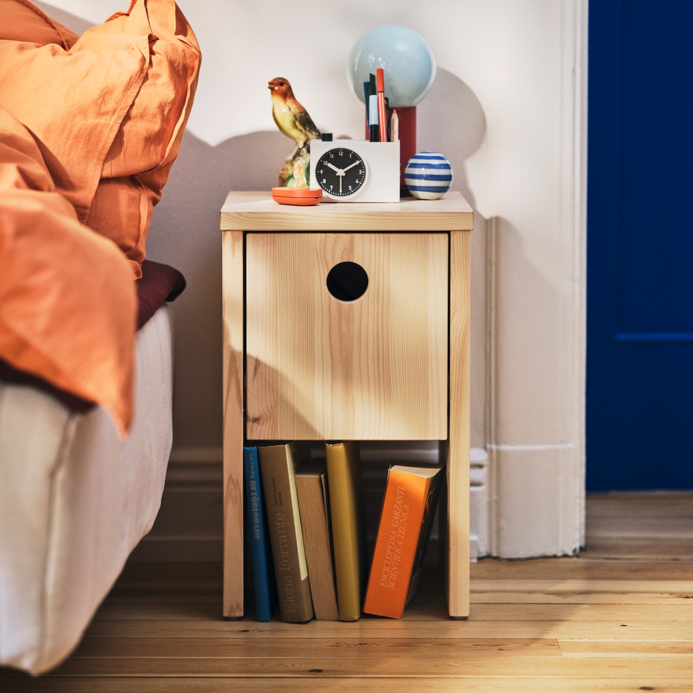 Ett IKEA PS 2026 sängbord i trä med en låda för förvaring och en hylla för böcker i en mysig sovrumsmiljö.
