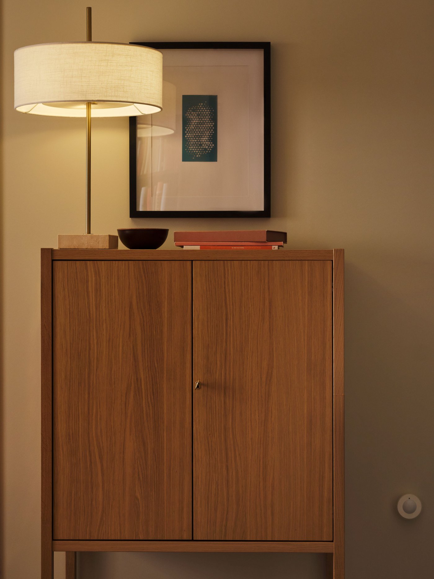 En trådlös rörelsesensor, MYGGSPRAY, är monterad på väggen intill ett STOCKHOLM 2025‑skåp med två dörrar.