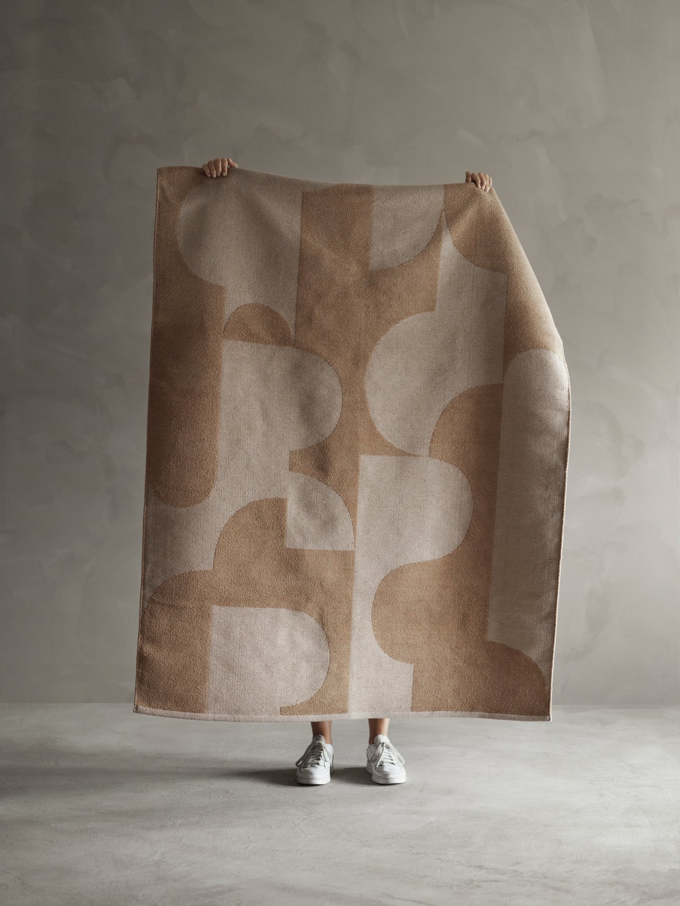 A person holding up a RÖDASK rug to show its bold, abstract print and jacquard weave.