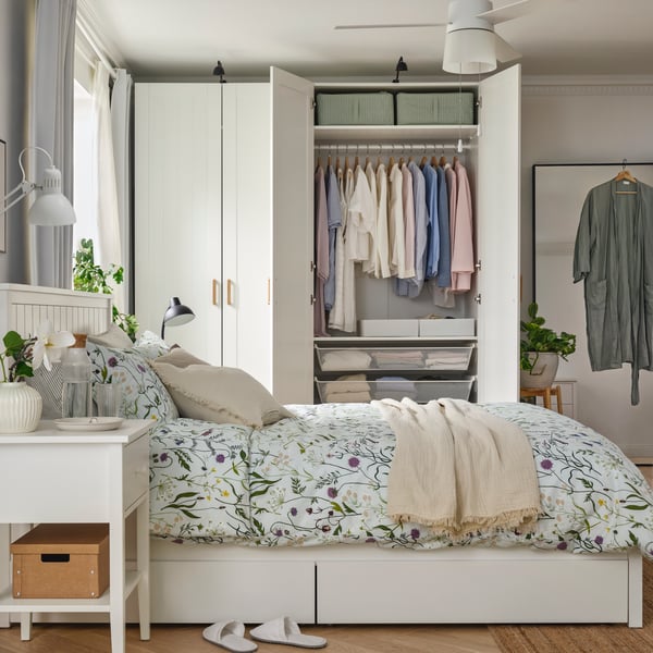 A bedroom with a PAX/GULLABERG wardrobe combination features open doors displaying neatly hung clothes and storage boxes.