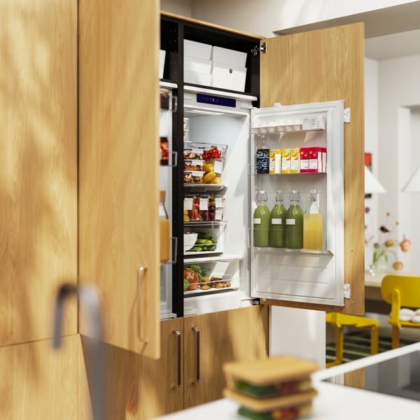 The doors of two ÖVERNÄS fridge/freezers with SINARP fronts in oak veneer are open, showing food items stored inside.