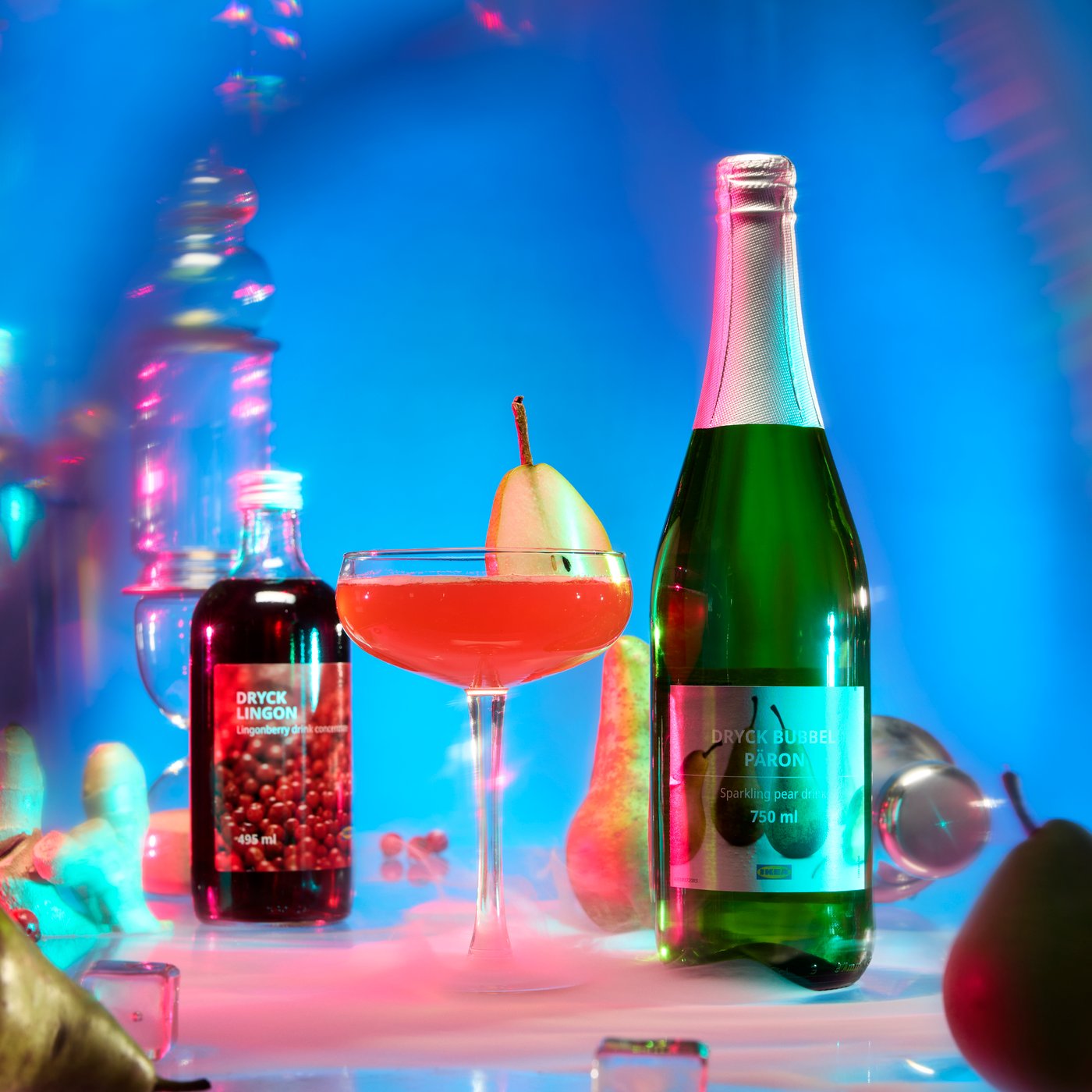 A glass with a red drink is placed between a bottle of DRYCK BUBBEL PÄRON and a bottle of DRYCK LINGON lingonberry syrup.