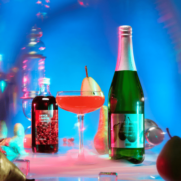 Et glass med rød drikke står mellom ei flaske DRYCK BUBBEL PÄRON og ei flaske DRYCK LINGON tyttebærsaft.