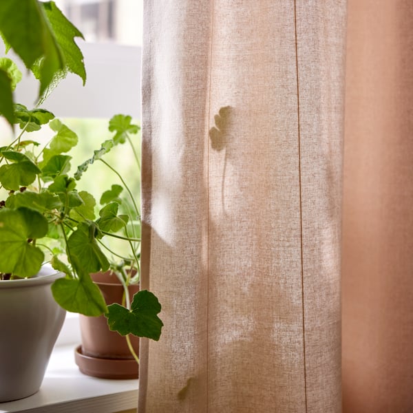 Beige gardiner med en grön krukväxt i bakgrunden.