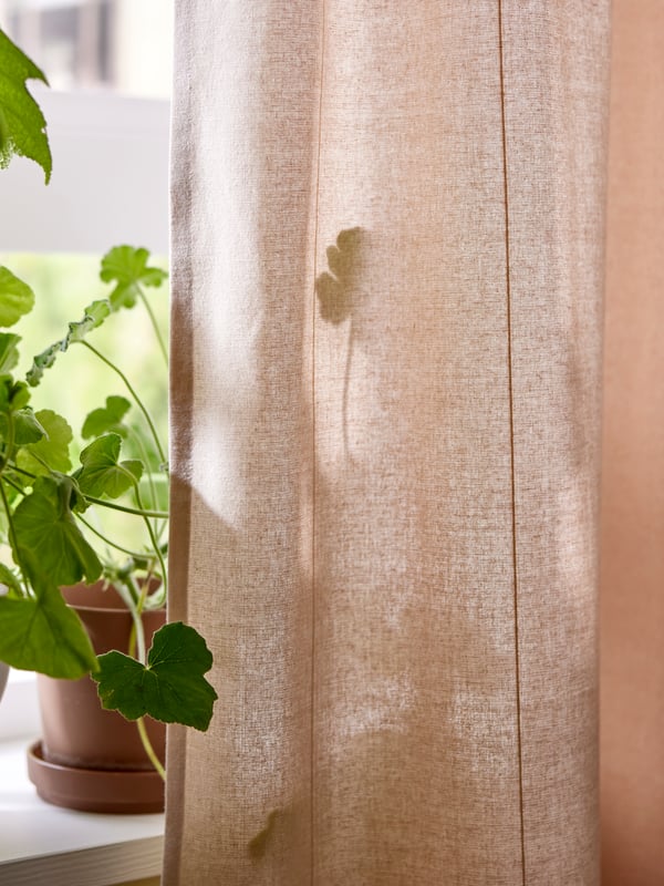 To plantepotter med planter står på en vinduskarm med en lyserosa LENDA gardin hengende på den ene siden av vinduet.
