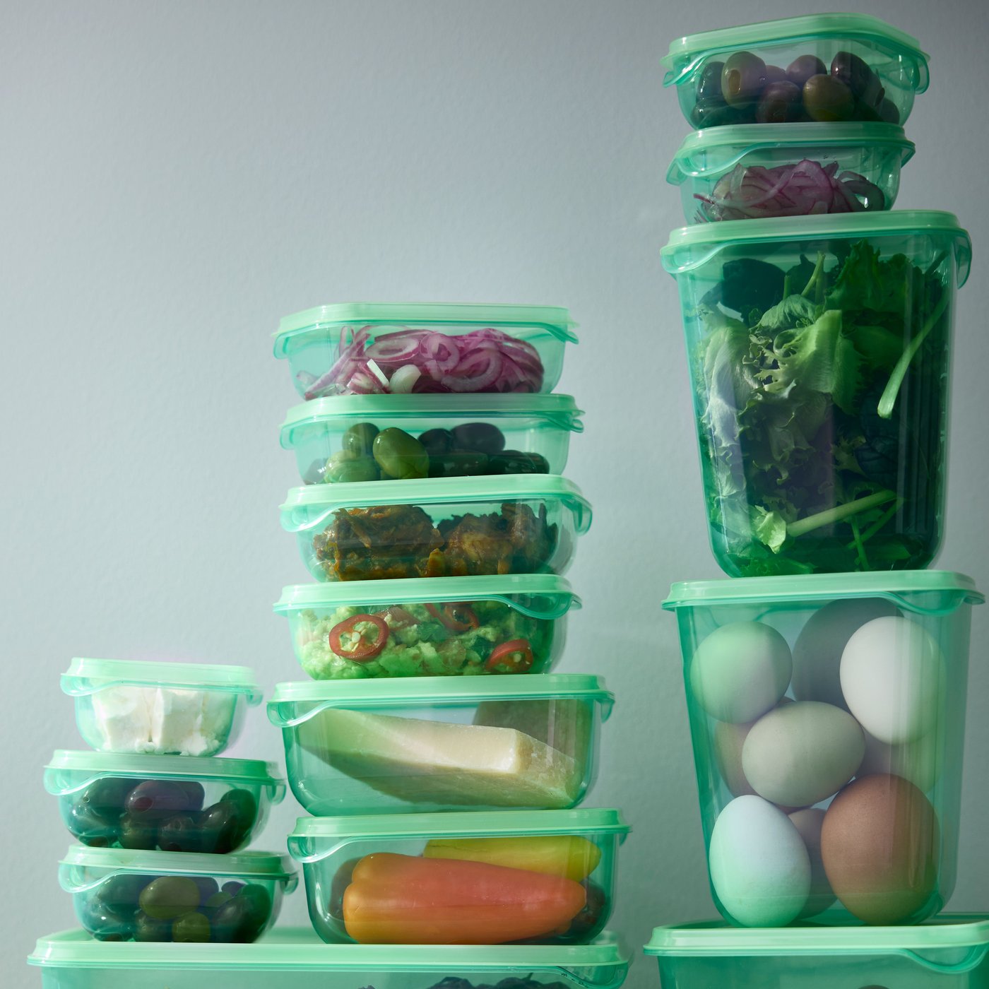 17 green PRUTA food containers with lids, with tortilla chips, eggs, vegetables, and bread, are stacked on top of each other.