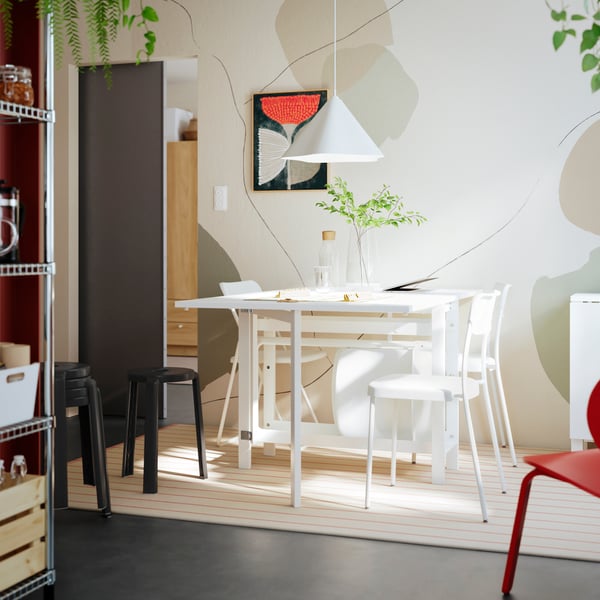 A bright dining area featuring a white dining table with two chairs and a black bar stool, surrounded by light tones.