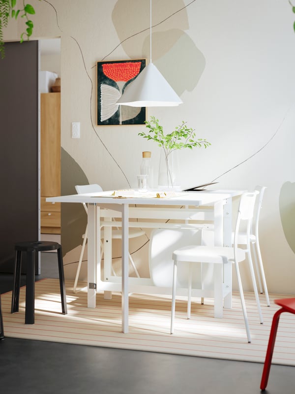 A bright dining area featuring a white dining table with two chairs and a black bar stool, surrounded by light tones.