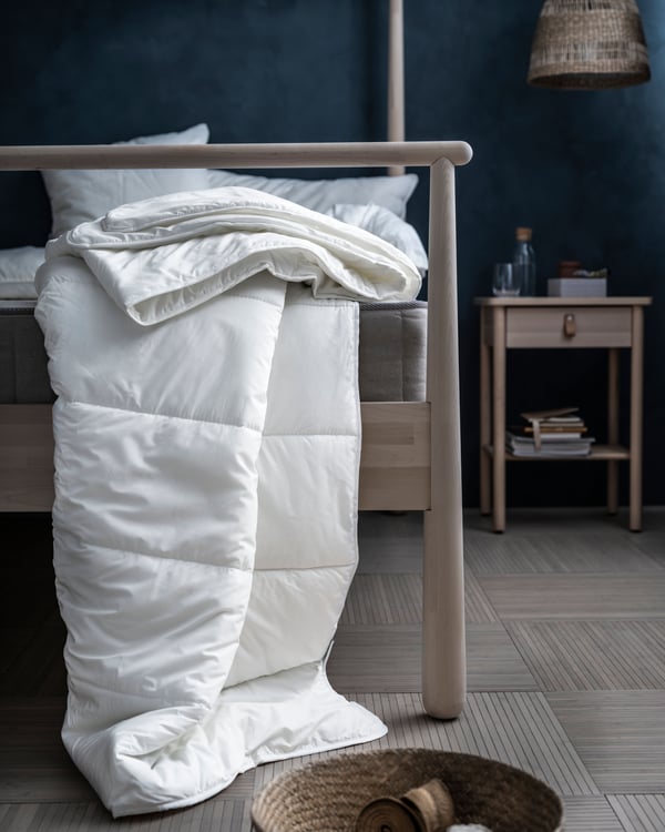 Bedroom with a white duvet draped from the foot end of the GJÖRA bed frame down to the wooden floor. BJÖRKSNÄS bedside table.