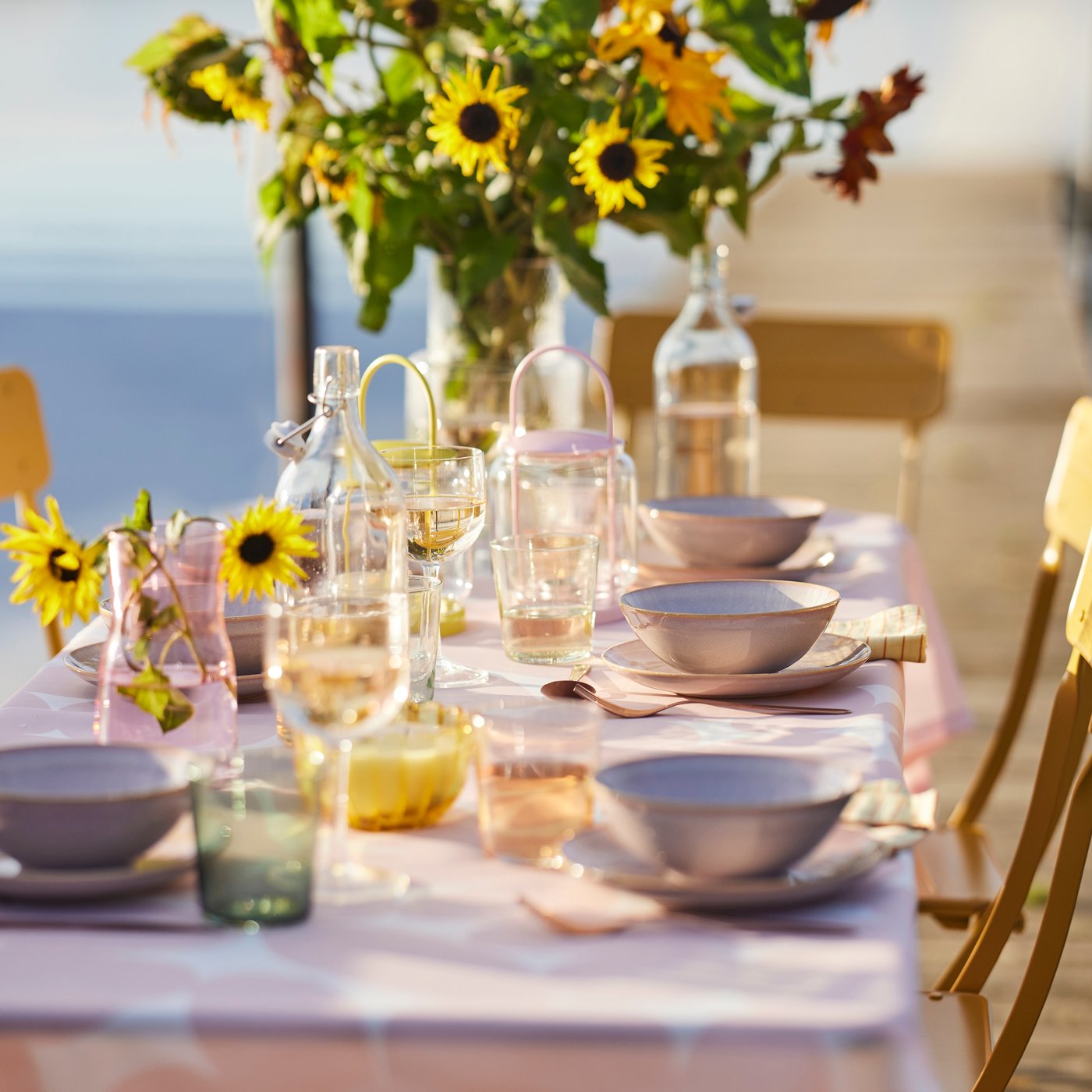 Ett utomhusdukat bord för en drömmig sommarfest vid en sjö, med TOFSAND-duk med ett ljusrosa mönster.