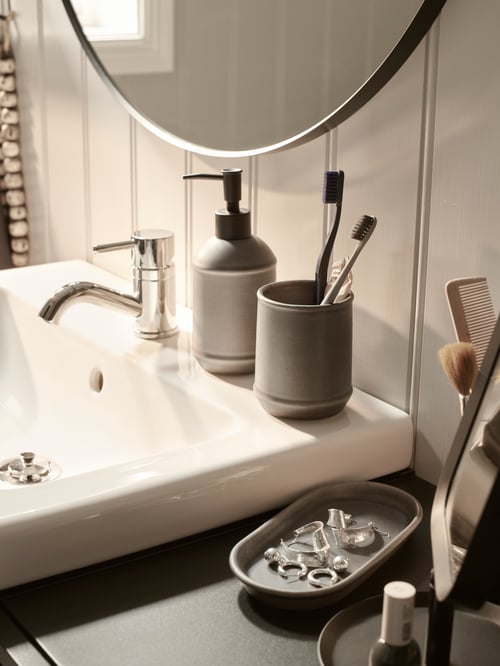 A TVÅLSJÖN soap dispenser and toothbrush mug at the back of a wash basin, with the tray holding jewellery beside it.