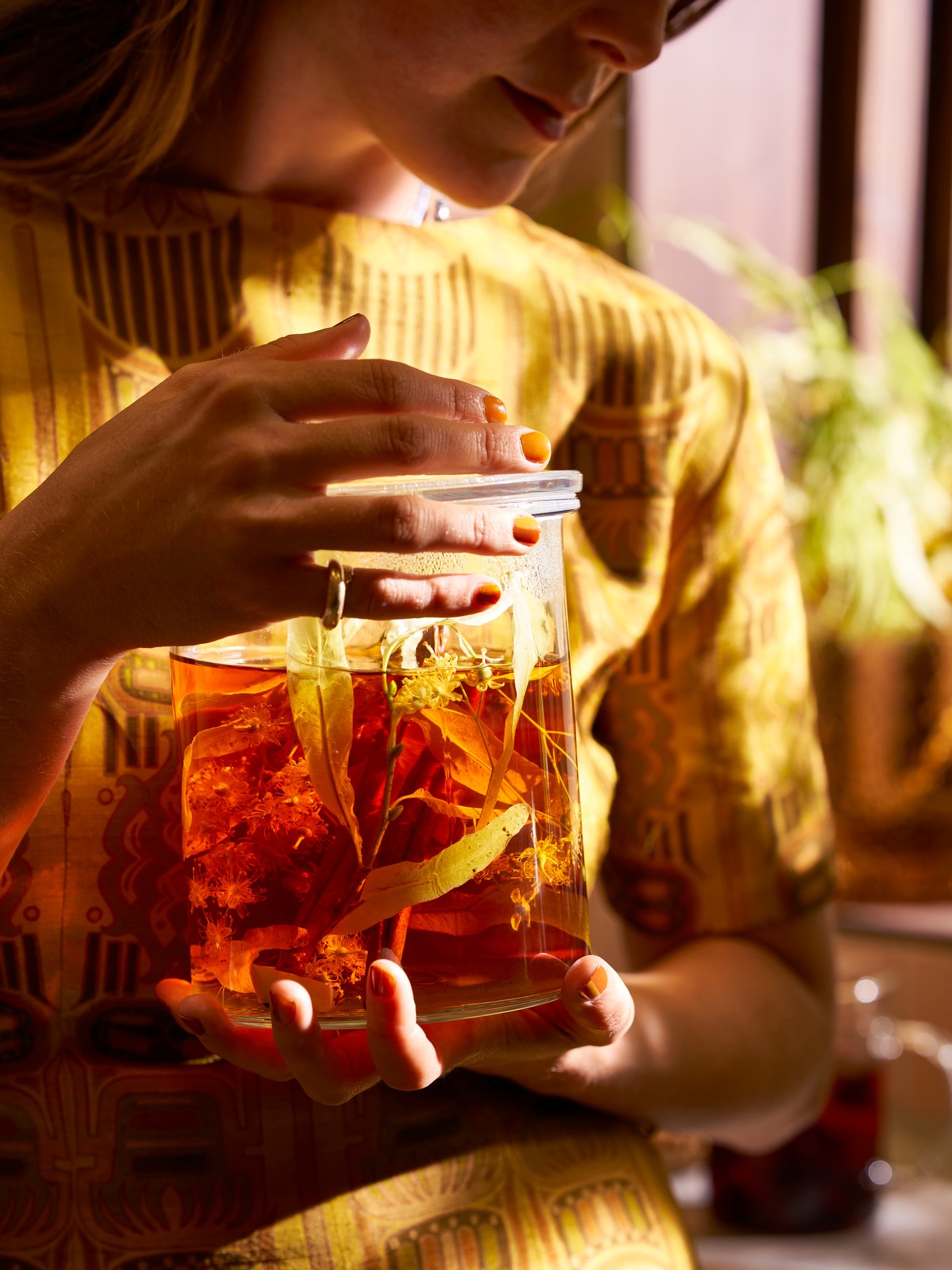 A person wearing a yellow jumper is holding on to an IKEA 365+ glass jar with lid filled with a herbal water infusion.