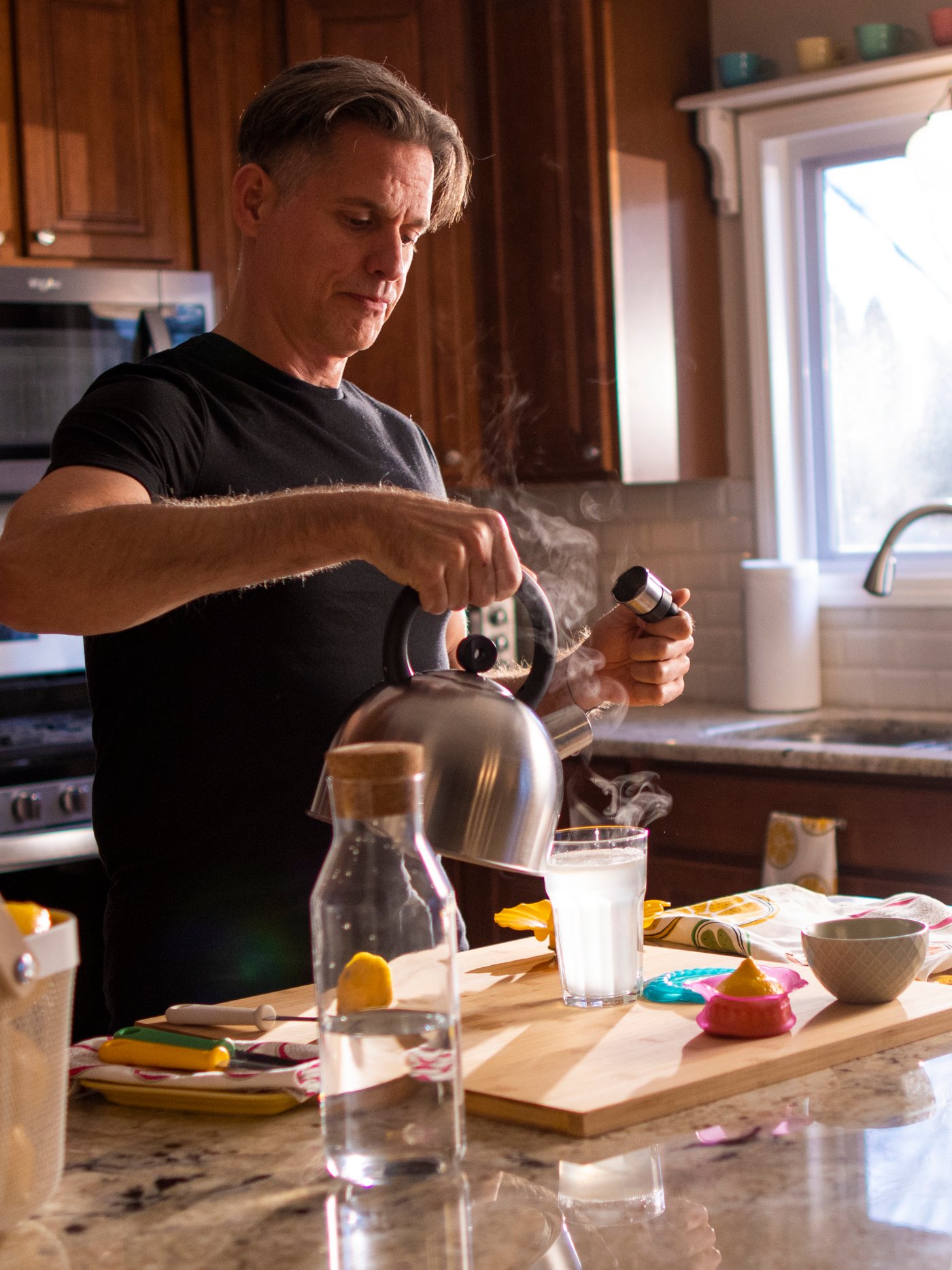 Un homme qui prépare une boisson avec du jus de citron frais dans une cuisine remplie de lumière naturelle.