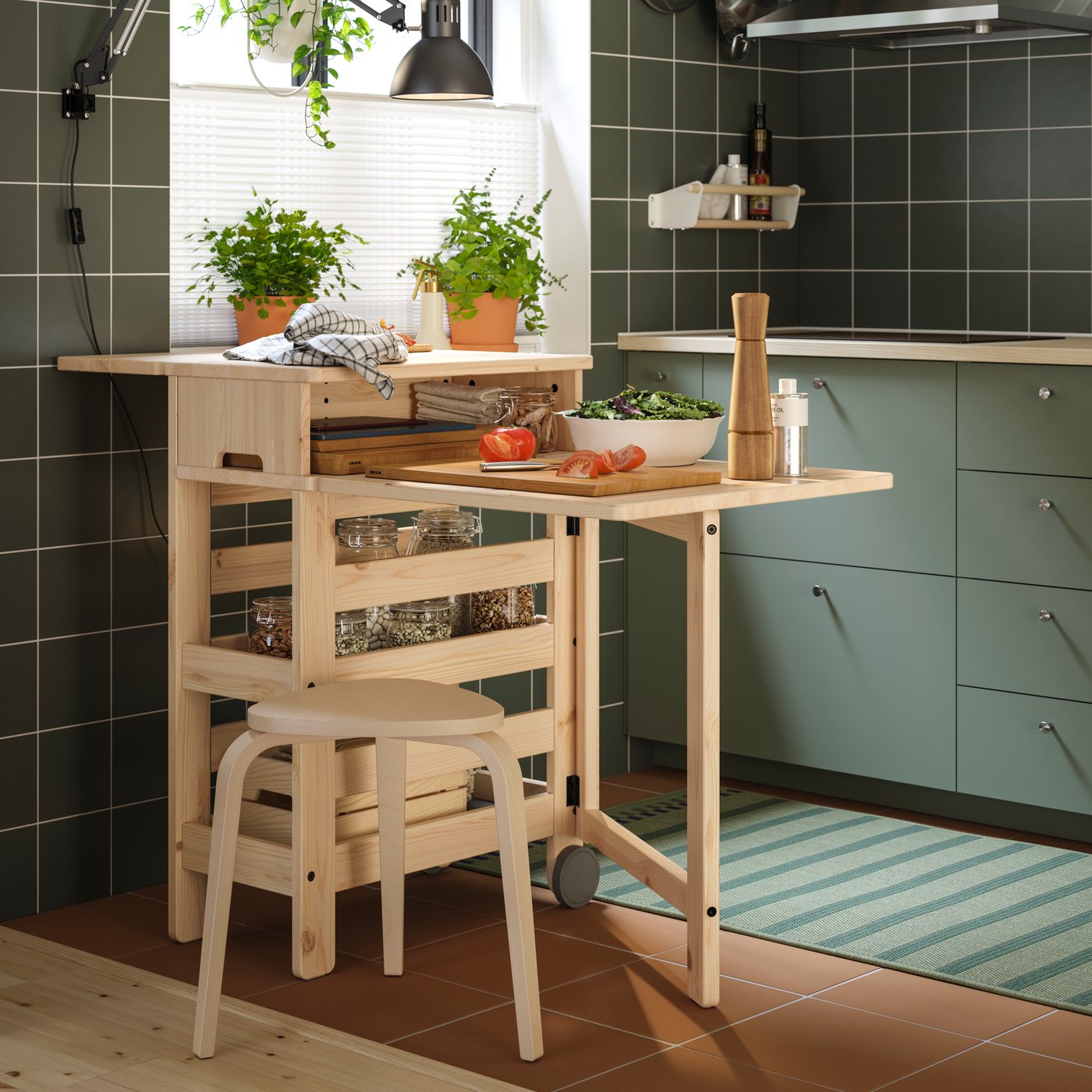 Et flytbart RESARÖ klapbord med opbevaring står i et køkken med køkkenudstyr ovenpå og en barstol ved siden af.