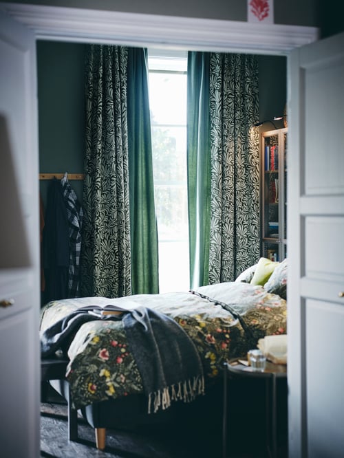 Schlafzimmer mit TRÅGSPINNARE Gardinenschals, einem GLADOM Tabletttisch, der KÄRRDUNÖRT Bettwäsche und einem ULLTISTEL Plaid.