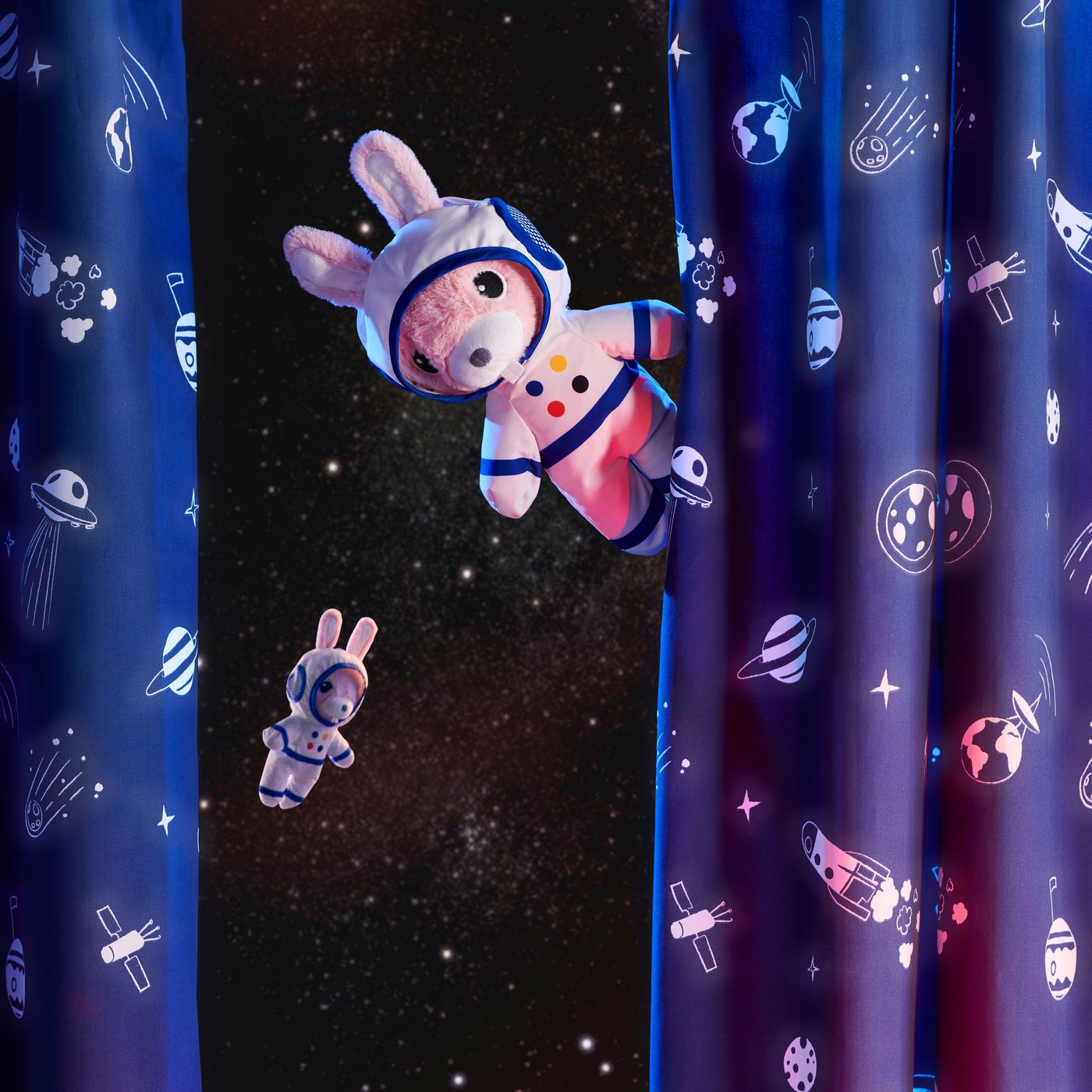 Plyšový astronaut AFTONSPARV vykukuje vedle závěsu s vesmírnou tématikou. V pozadí je vesmír.