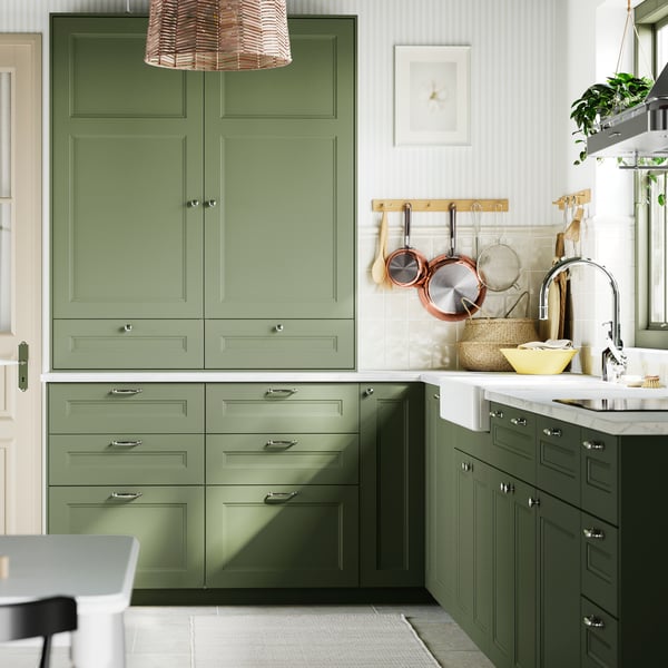 A kitchen with AXSTAD grey-green fronts, brightened by natural light, complemented by white tiles and wooden accents.
