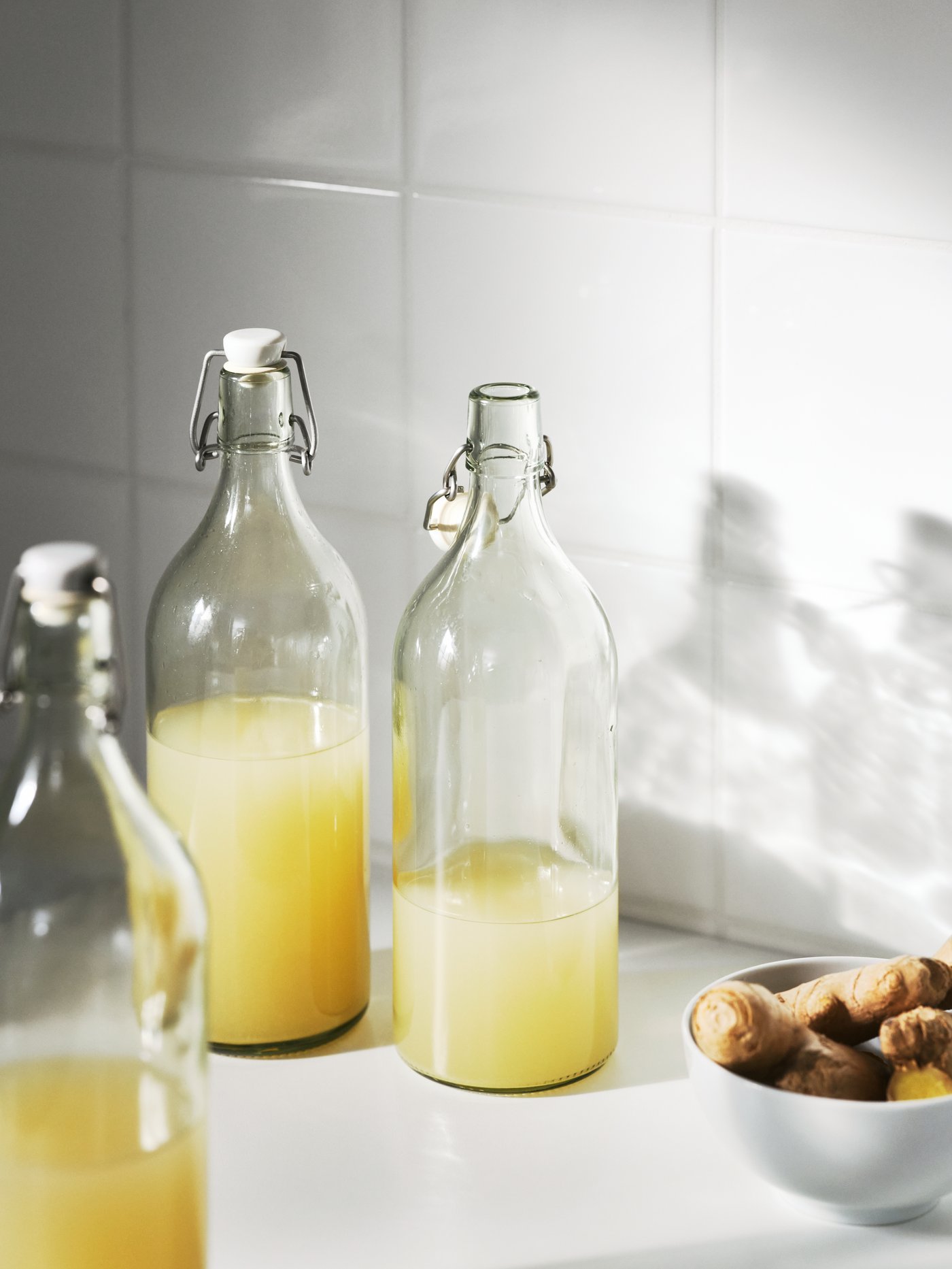 Detalle de varias botellas blancas transparentes con tapón de vidrio incoloro, junto a un cuenco blanco.