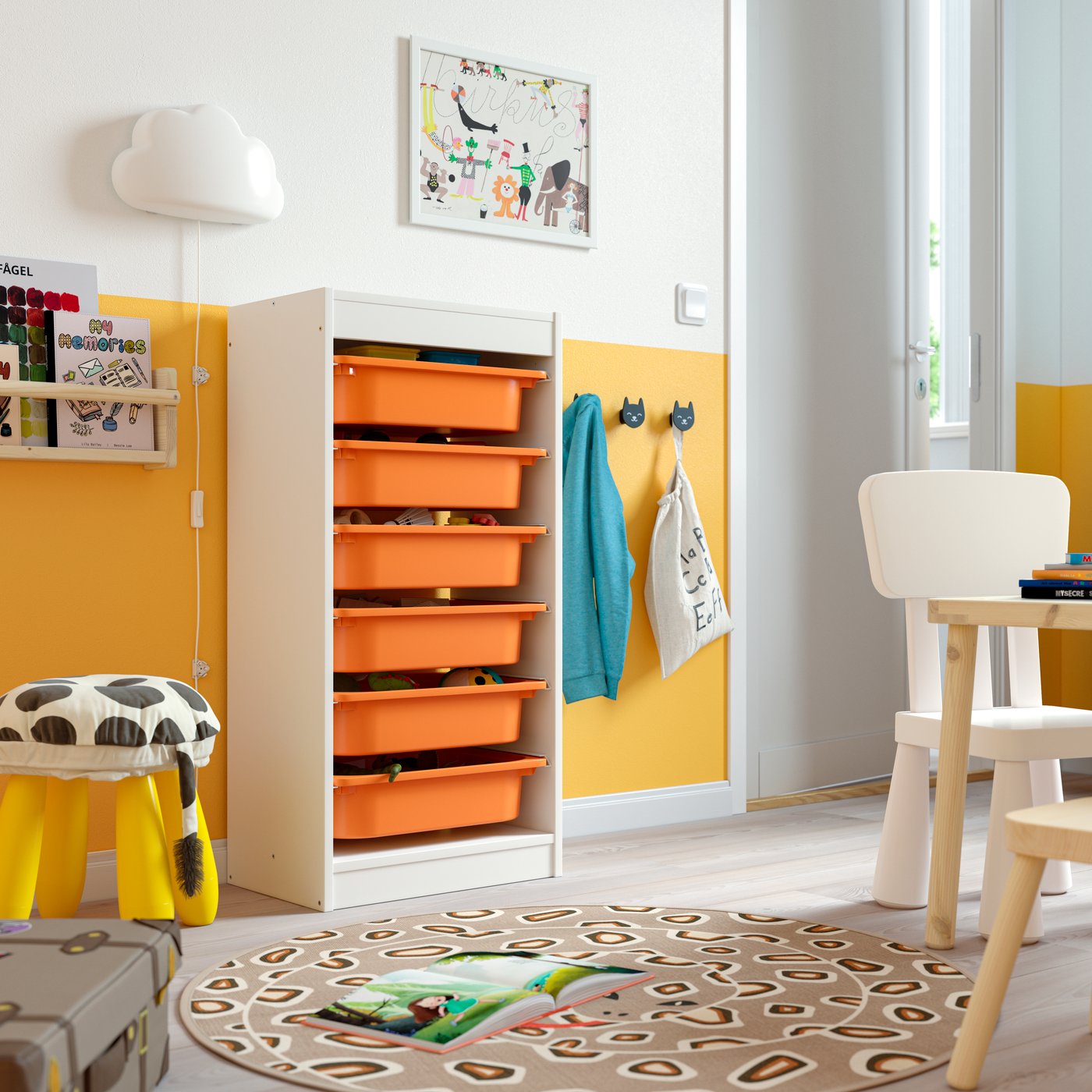 Speelhoek met witte kast en oranje bakken, kapstok met jasjes en tas, stoel en tafel op kleurrijk tapijt in lichte kinderkamer.
