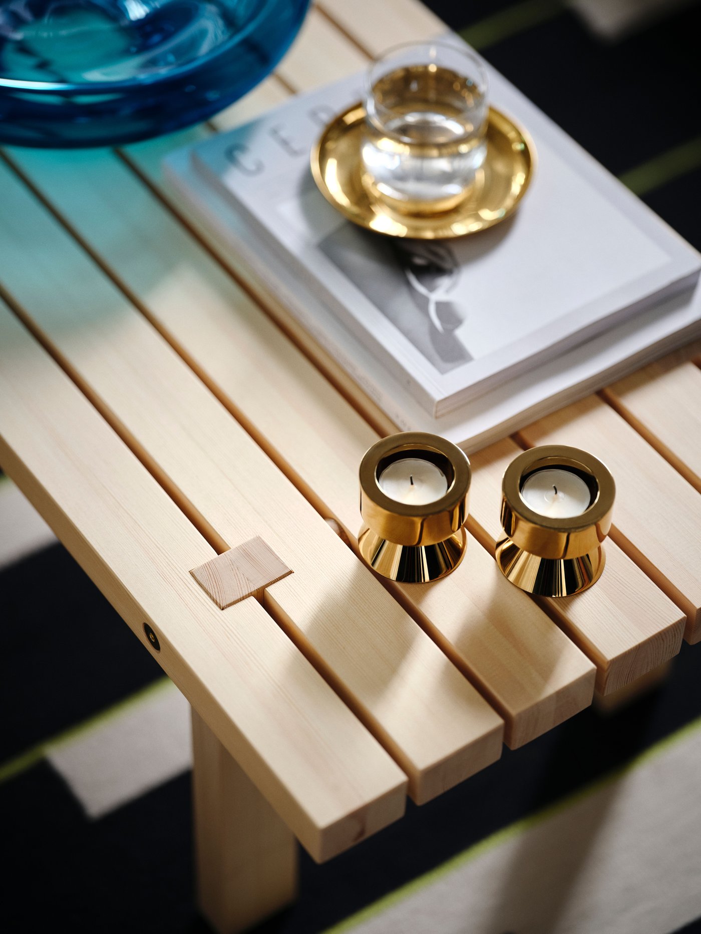 Et STOCKHOLM 2025 sofabord i træ med messingfarvede lysestager/fyrfadsstager, en skål og andre ting på.