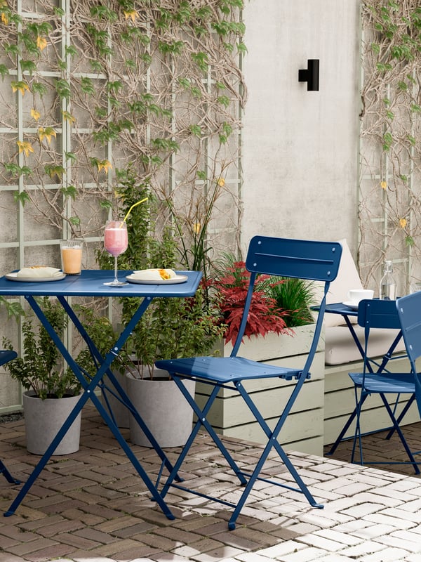À l'extérieur, une table et deux chaises pliantes d'extérieur SUNDSÖ bleu foncé/bleu foncé.