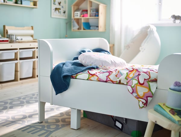 White BUSUNGE extendable child's bedframe in the bedroom with VITHAMINER HJARTA colourful bedsheets and TROFAST storage cabinets in the bedroom.