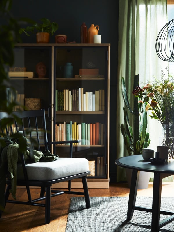 A PERSBOL armchair and a black KRAGSTA coffee table stand in front of a grey-brown LANESUND glass-door cabinet.
