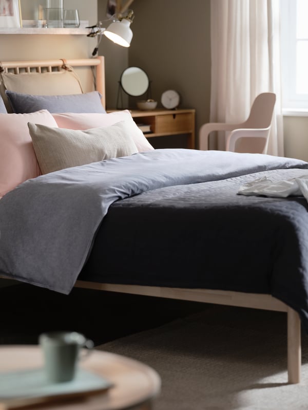 Una recámara con una cama de abedul BJÖRKSNÄS, ropa de cama KOPPARBLAD azul oscuro, un tocador NORDKISA y una silla giratoria ODGER.