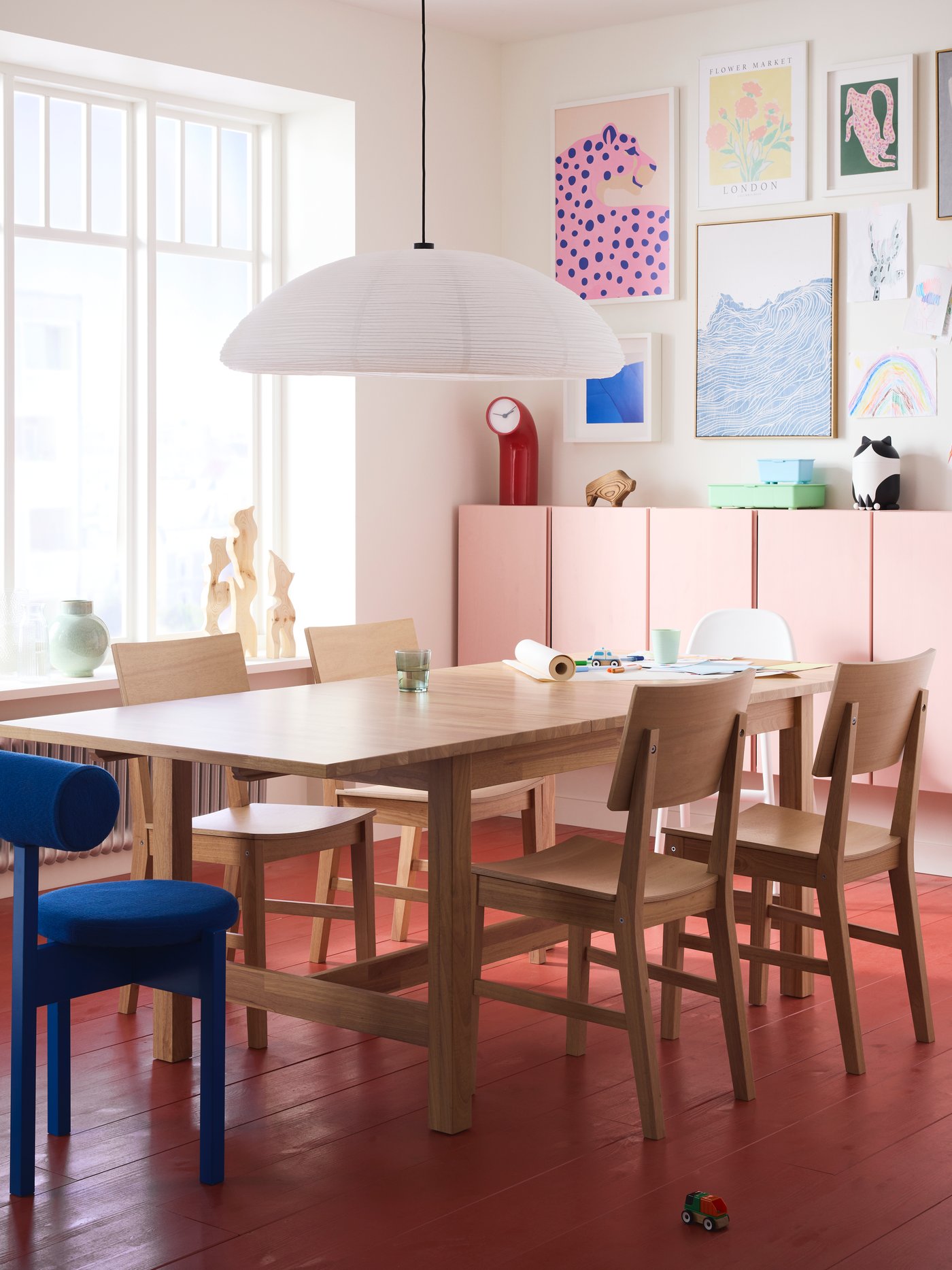 A bright dining area with a red floor features a KARSKÄR extendable table and chairs and colourful artwork on the wall.