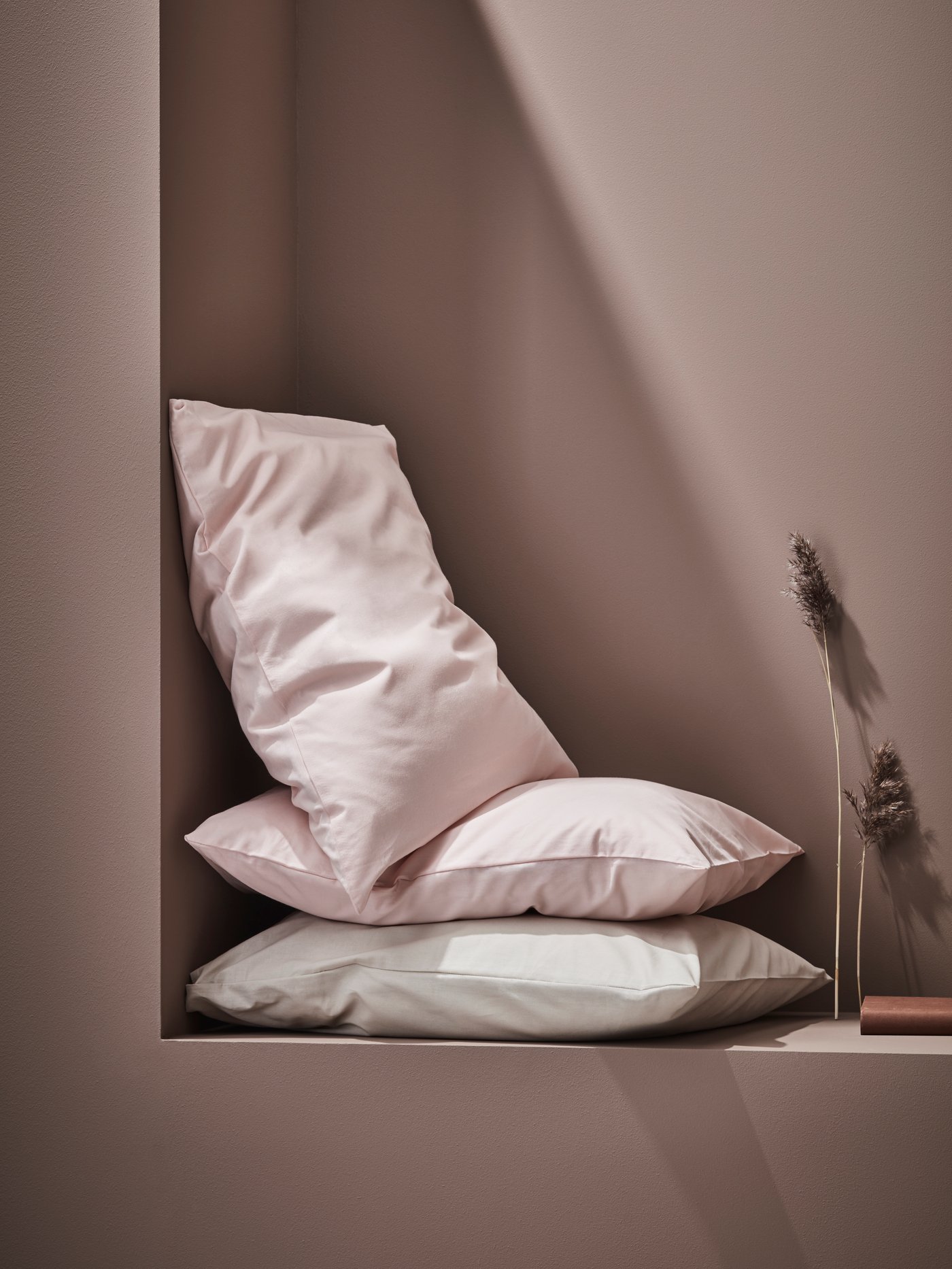 Dormitorio moderno con tres almohadas de color rosa claro y fundas de almohada verde claro junto a accesorios de plumas.