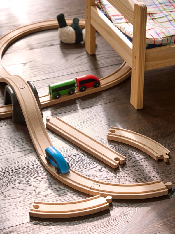 Close-up of LILLABO train set with rails and toy figures, built next to DUKTIG doll's bed.