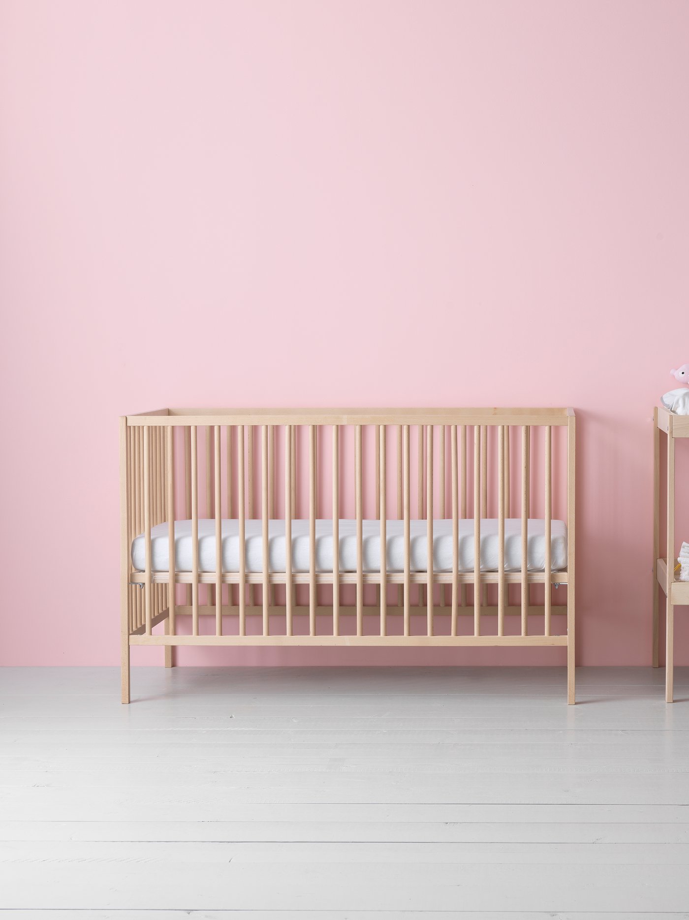 Beech SNIGLAR baby crib against a pink wall.