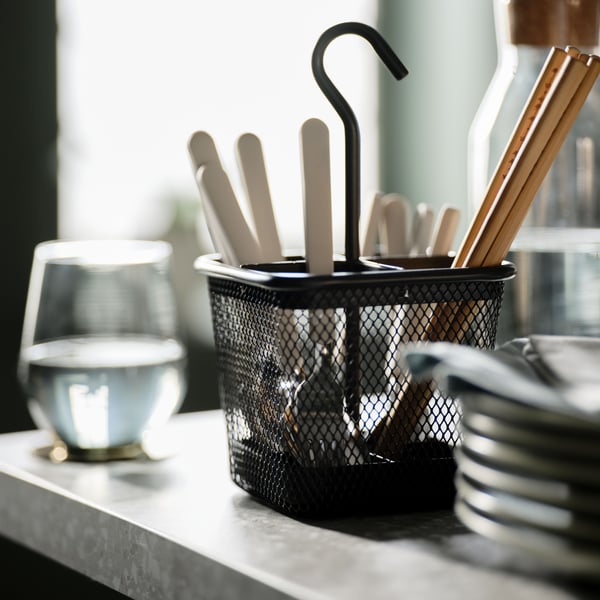 Bamboo TREBENT chopsticks and beige UPPHÖJD cutlery in an anthracite-colour UPPDATERA cutlery caddy on a grey worktop.
