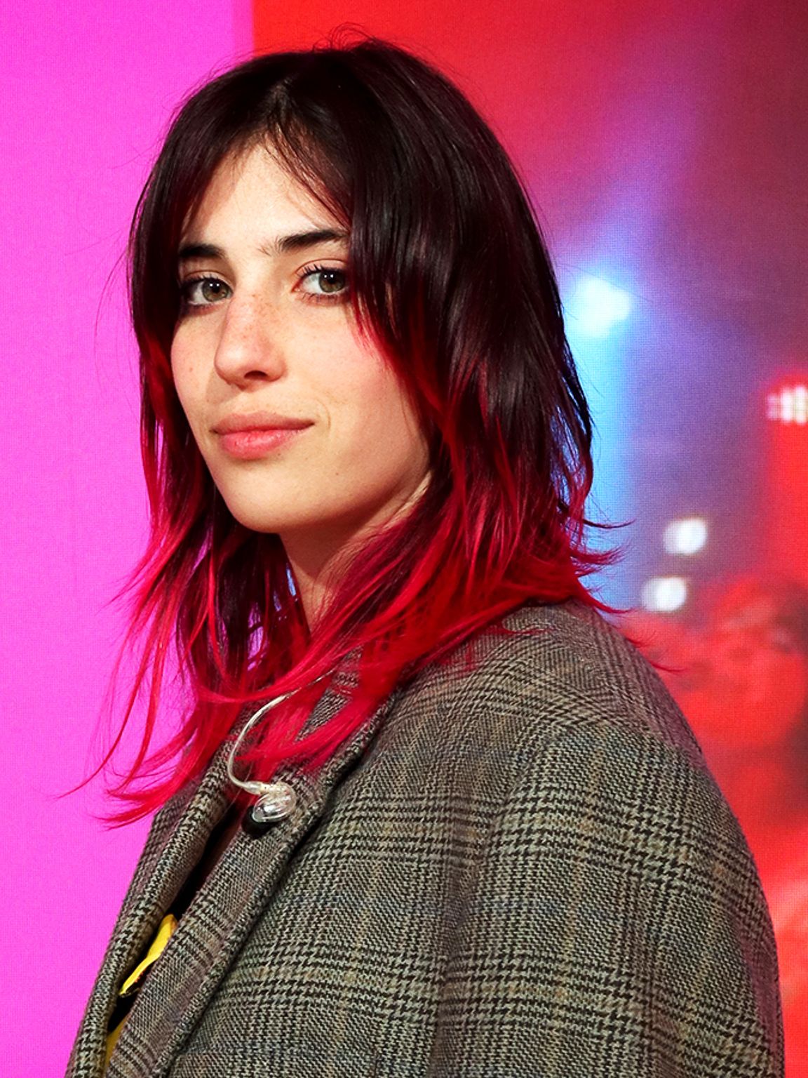 Chiamamifaro stoji na odru pred ozadjem rožnate barve, za ozadje poskrbi digitalni zaslon, ki se med milanskim tednom oblikovanja 2024 uporablja na odru prizorišča IKEA. 