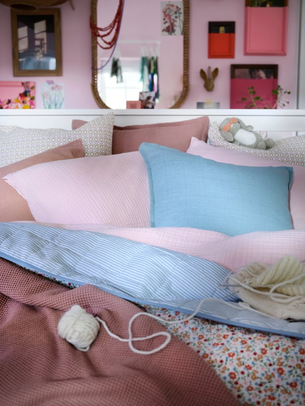 Close-up of white bed with bedding and extra cushions in light pink, dark pink, blue and a flower pattern.