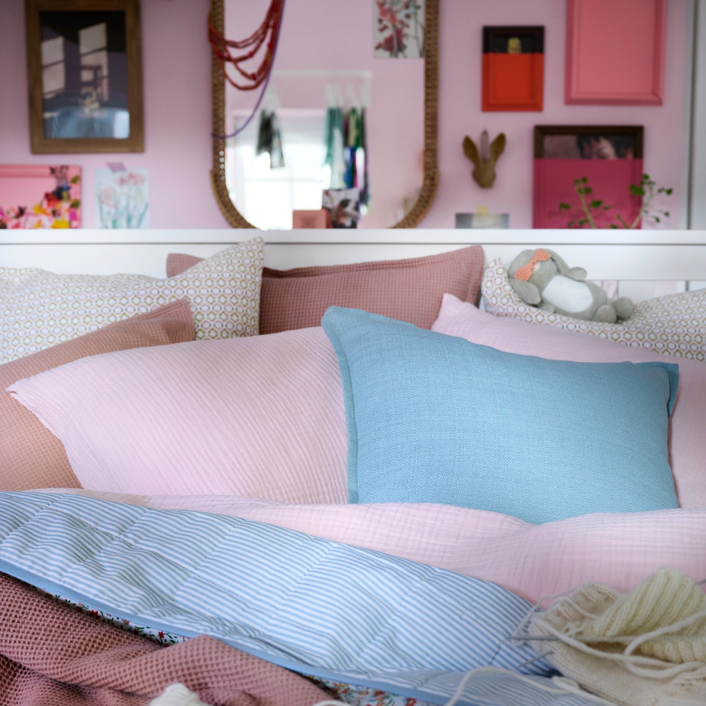 Close-up of white bed with bedding and extra cushions in light pink, dark pink, blue and a flower pattern.