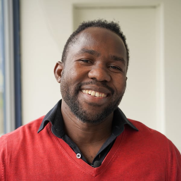A man standing on a balcony in a red shirt looking towards the camera smiling.