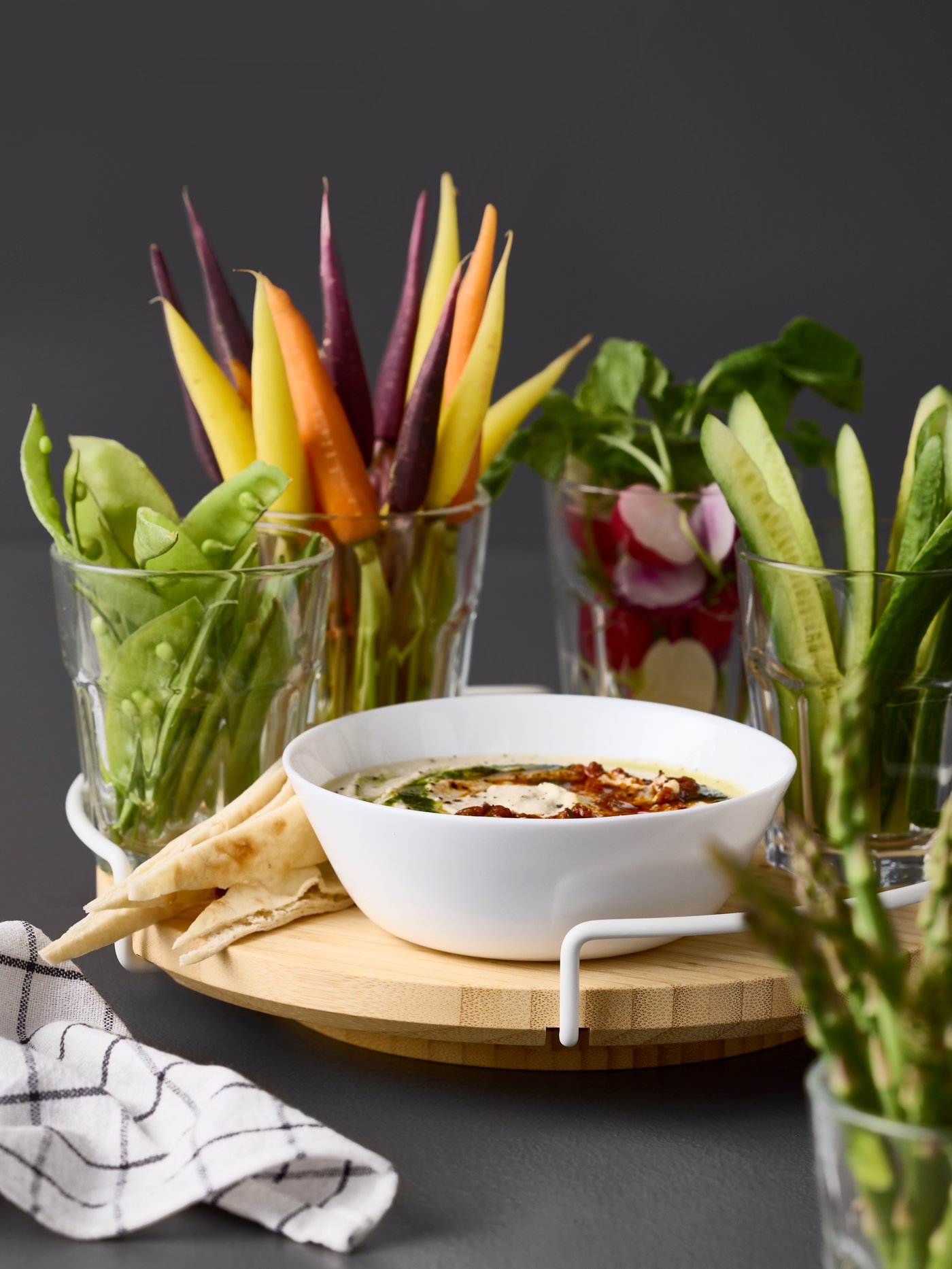 An APTITLIG lazy Susan in bamboo has four POKAL glasses with colourful vegetables and a white OFTAST bowl with a dip sauce.