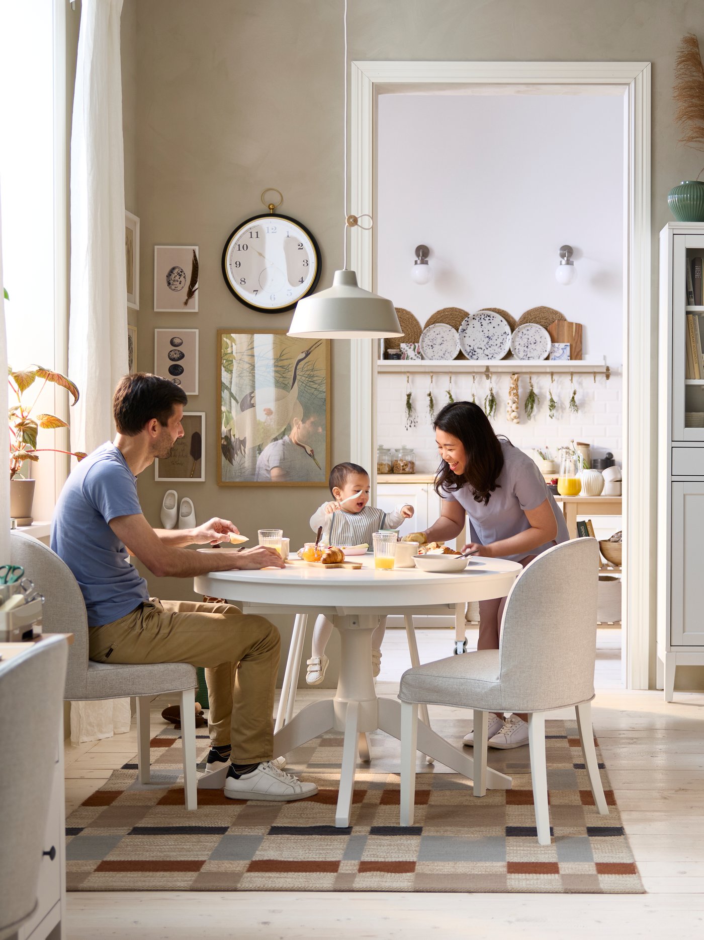 A dining area has a white ROSENTORP extendable table and two chairs, with a view of a kitchen area in the background.