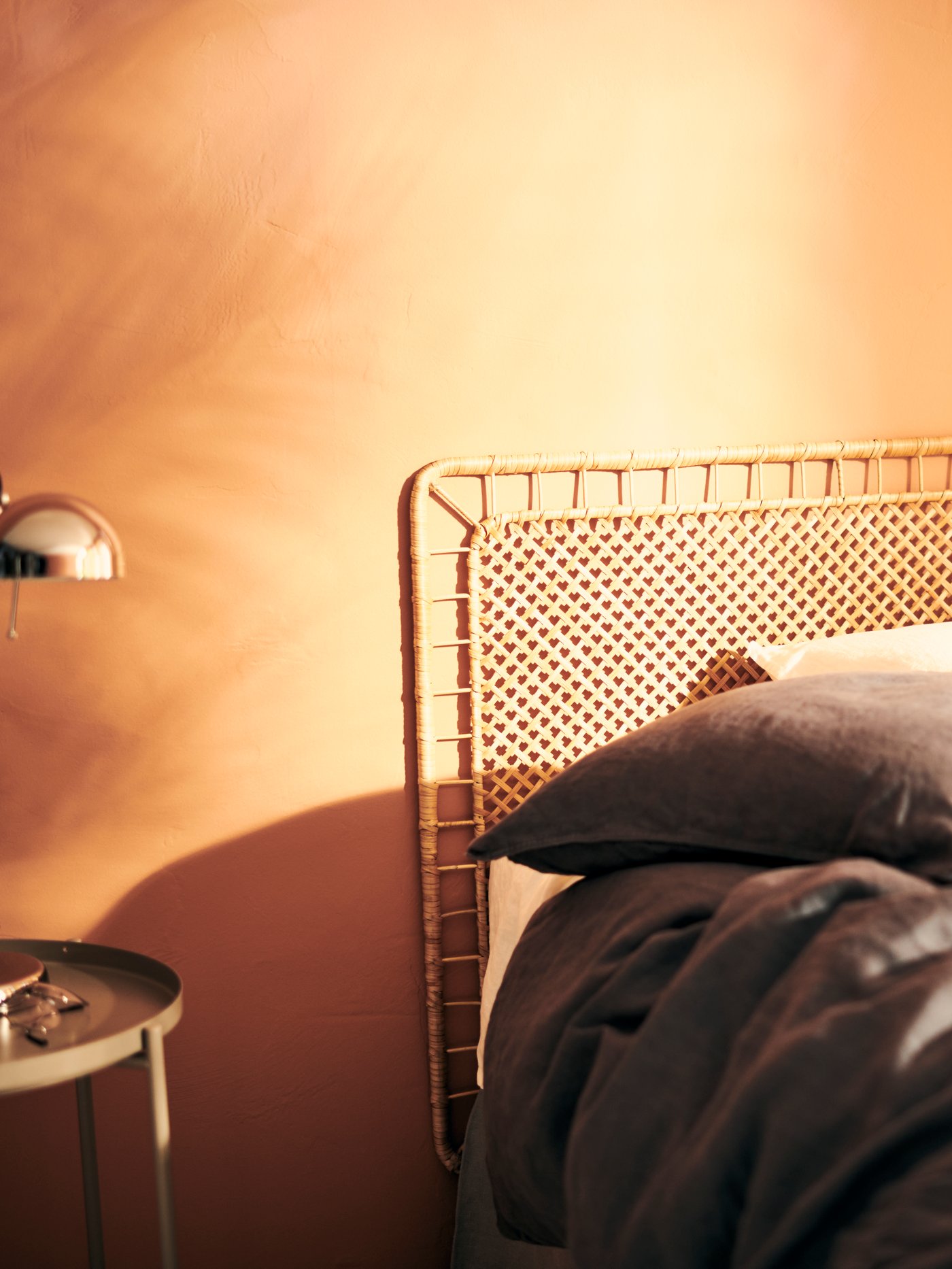 Una cama con ropa de ama gris. Resalta un respaldo de cama TOLKNING que contrasta con os tonos dorados de la pared