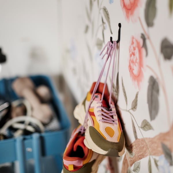 A HÖGAFFEL wall hook attached to a wall covered in flowery wallpaper holds a pair of colourful trainers by their laces.