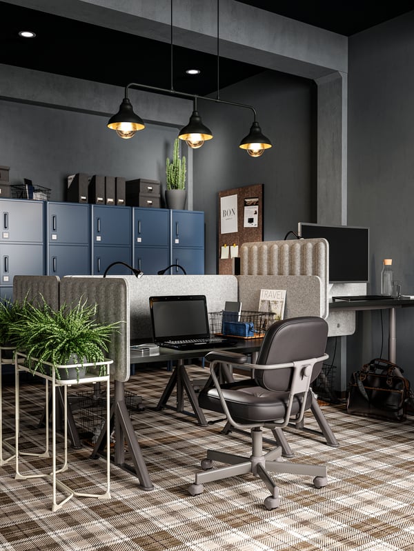 Workspaces divided by felt screens, a leather conference chair, a black laptop, three black pendant lamps, a plant.
