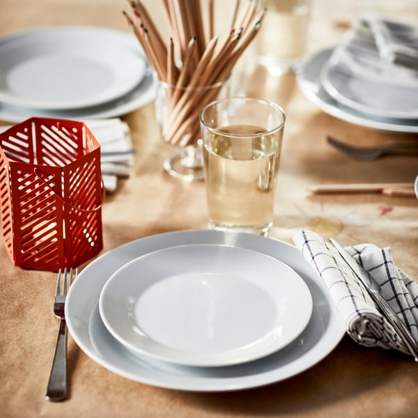 Tavolo apparecchiato con piatti bianchi, bicchieri IKEA 365+ e lanterna per candeline color corallo VÅRSYREN.