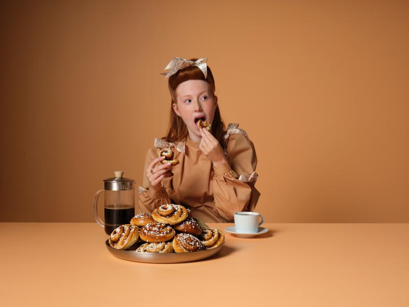 Eine Frau, die am Tisch sitzt und Zimtschnecken isst und Kaffee trinkt.
